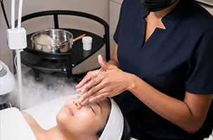 Steam rises while gloved hands massage the forehead at the start of a HydraFacial in North Dallas
