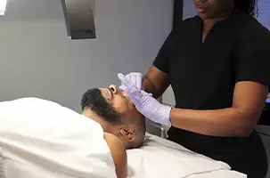 Esthetician performing a Hydrafacial Oak Lawn treatment on a male client resting on a treatment table