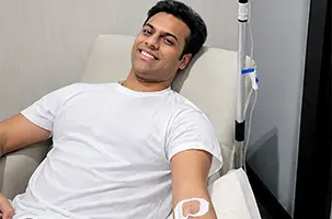 Young man grins from the recliner as his IV drip Preston infusion runs through the line above him